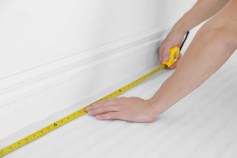 measuring room along white baseboards to prepare for carpet installation